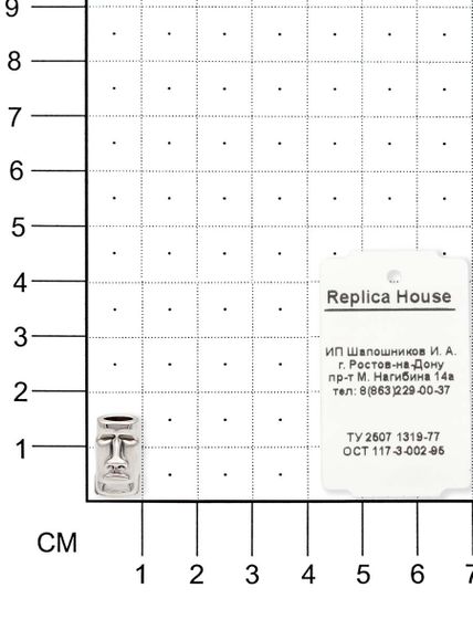 Фото шарма Моаи из серебра на размерной сетке с ювелирной биркой.
